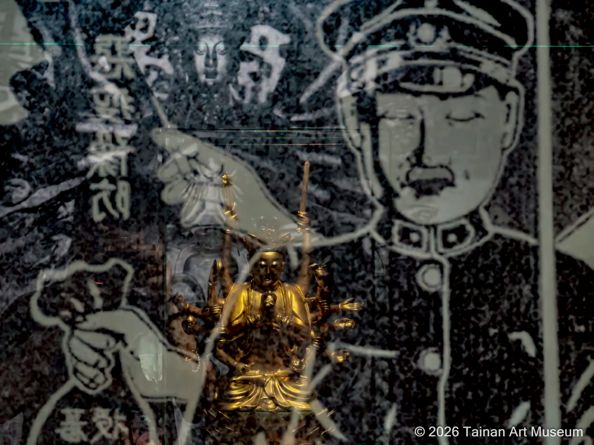▲搜查記入口特別集結〈清代木雕十八臂準提菩薩坐像〉、〈南無警察大菩薩〉海報，以及黃金樹的攝影〈準提菩薩〉三件作品，透過視覺穿透的展場設計，在同一視線中交錯呈現，也傳達出展覽其中一重要概念「錯訊」。（圖／南美館提供）